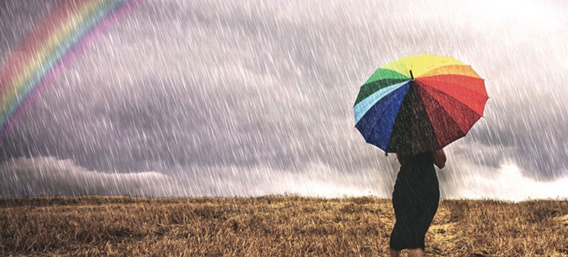 एक छतरी के साथ एक महिला बारिश में खेत में चलती है।  बाईं ओर एक इंद्रधनुष है।  फोटो: डब्लूएमओ